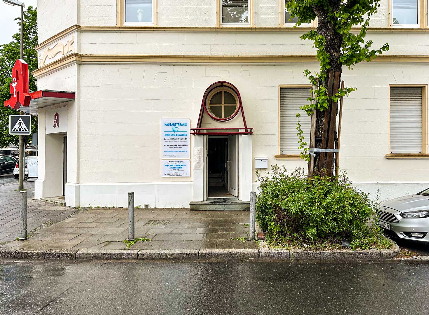 Foto zeigt die Eingangstür der Praxis an der Rahmer Straße 6 in Dortmund-Huckarde. Auf dem Foto ist auch die "Dorf-Apotheke" zu sehen, die sich im Erdgeschoss befindet. 